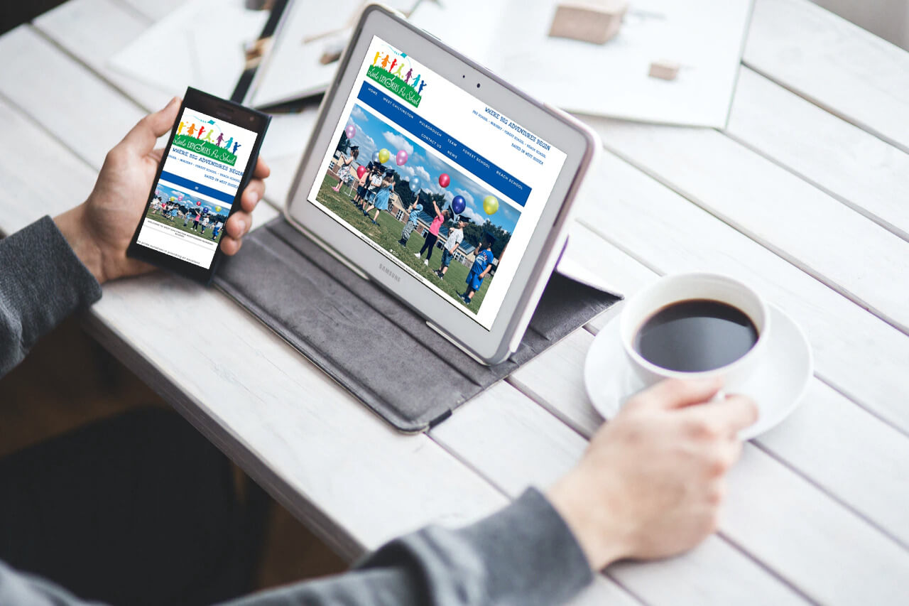 Little Explorers website displayed on a tablet and phone next to coffee cup